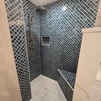 A walk-in shower with dark diamond-patterned mosaic tiles, a rainfall showerhead, built-in wall niche, and corner bench.