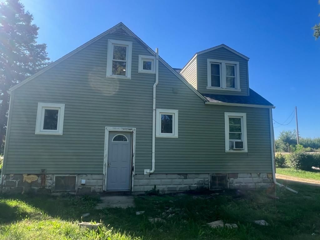 A two-story house with green vinyl siding, a gray door, and a dormer window, set against a clear blue sky.