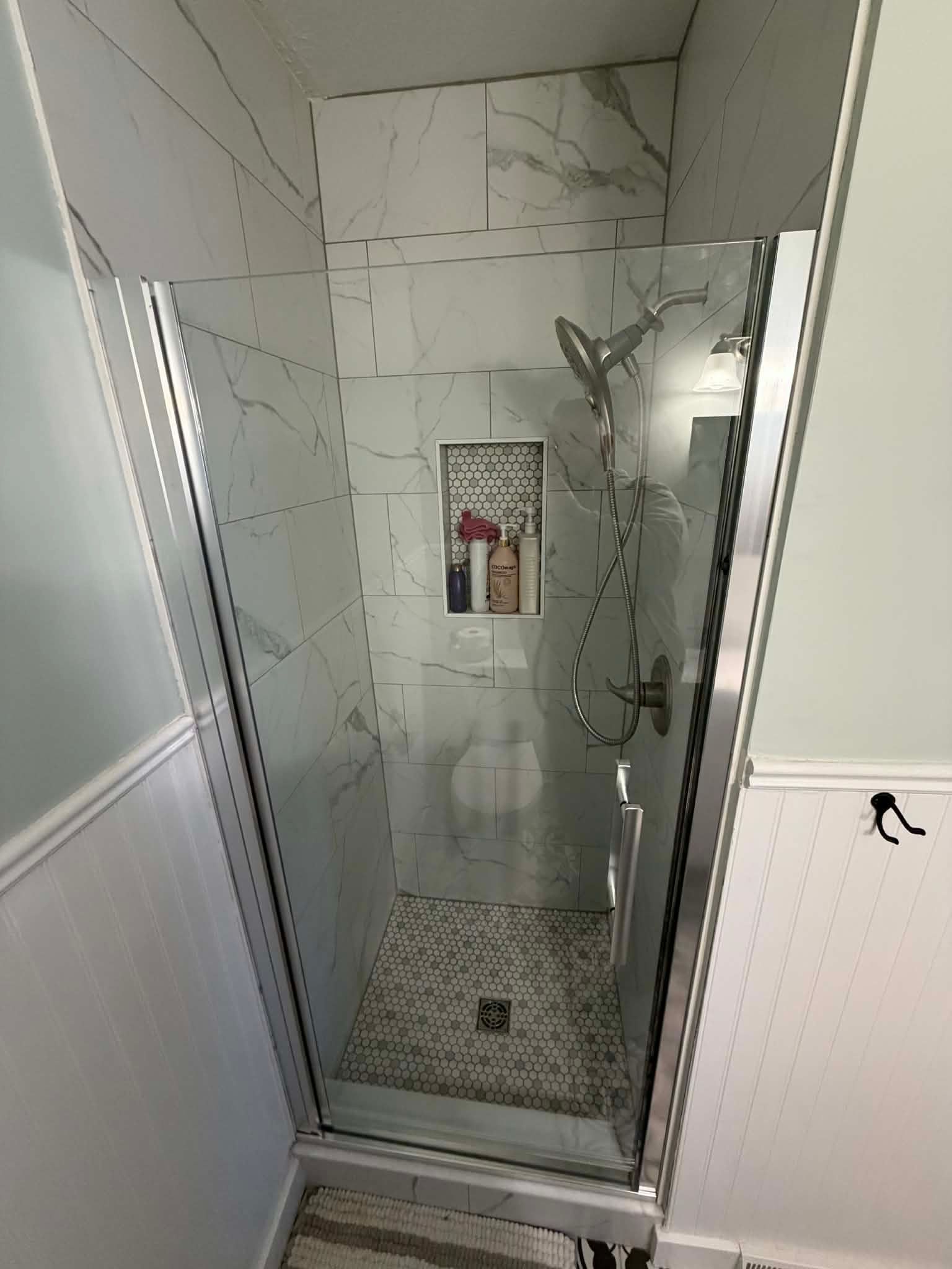 A walk-in shower with white marble-patterned wall tiles, a decorative patterned niche, and a glass-paneled door.