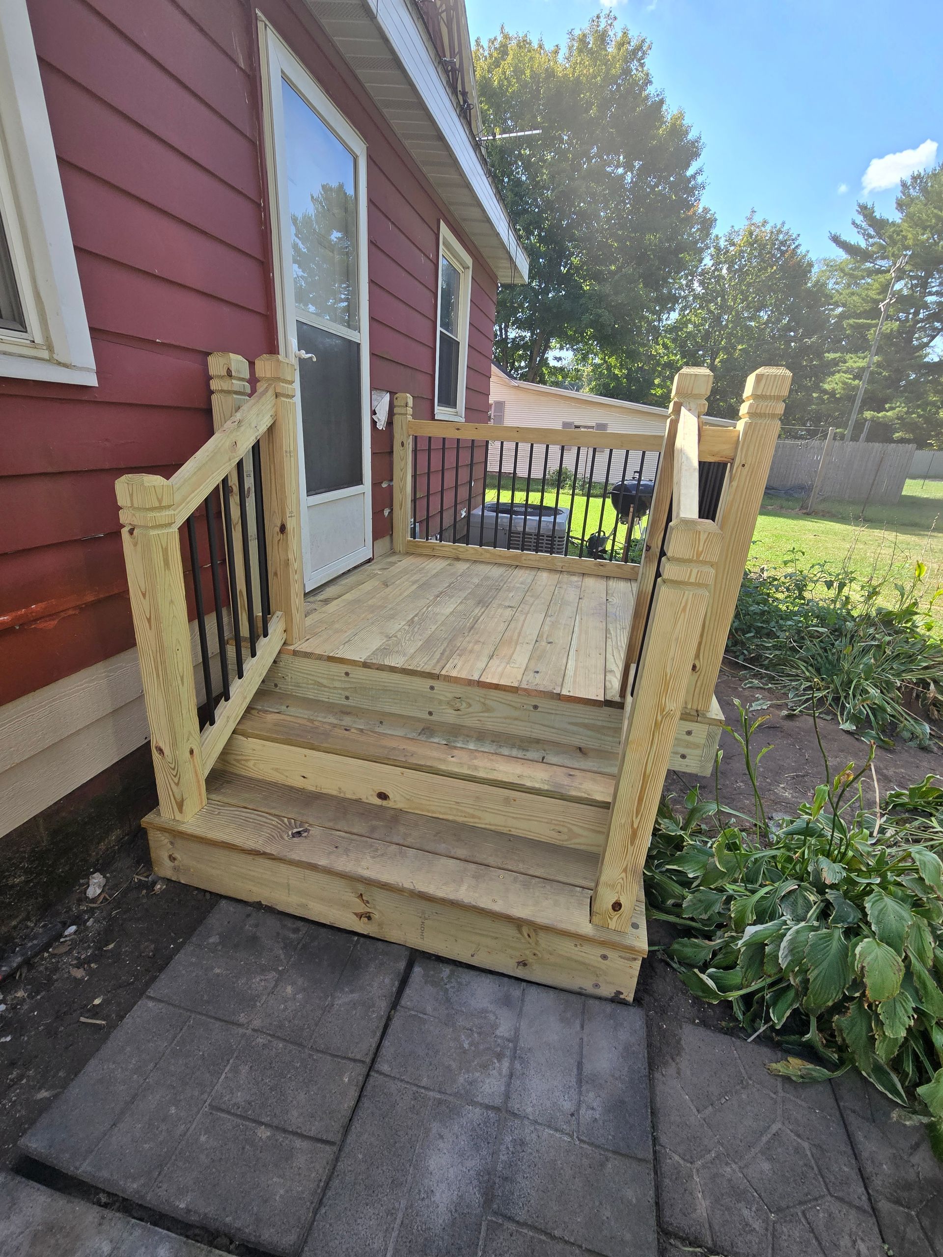 A newly constructed wooden deck and stairs with railings attached to the back entrance of a red-sided house.