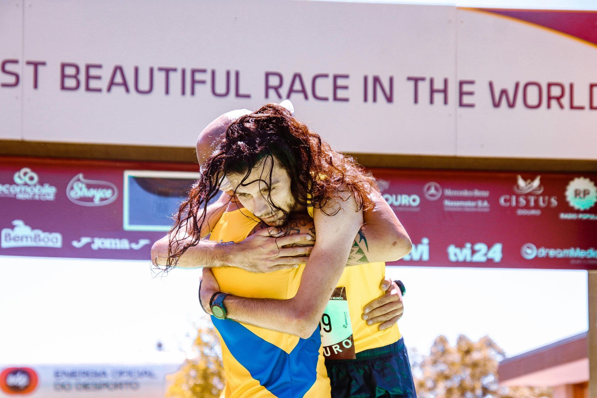 Two people hugging in front of a sign that says ' most beautiful race in the world '