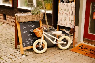 A white bicycle with a basket is parked in front of a store.