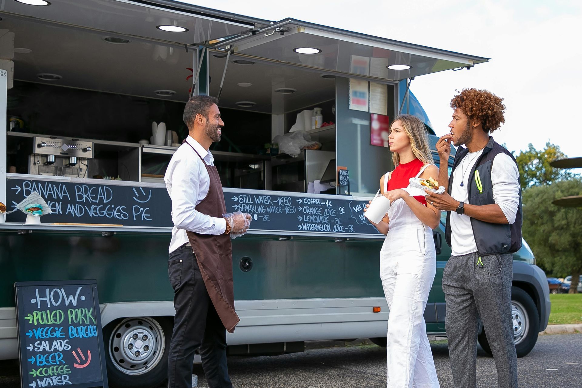 Food truck worker serving two customers outdoors.