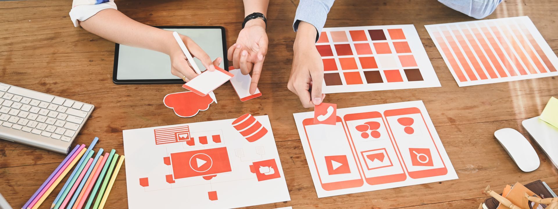Hands on swatches of colored fabric on a white table with a tablet and notebook.