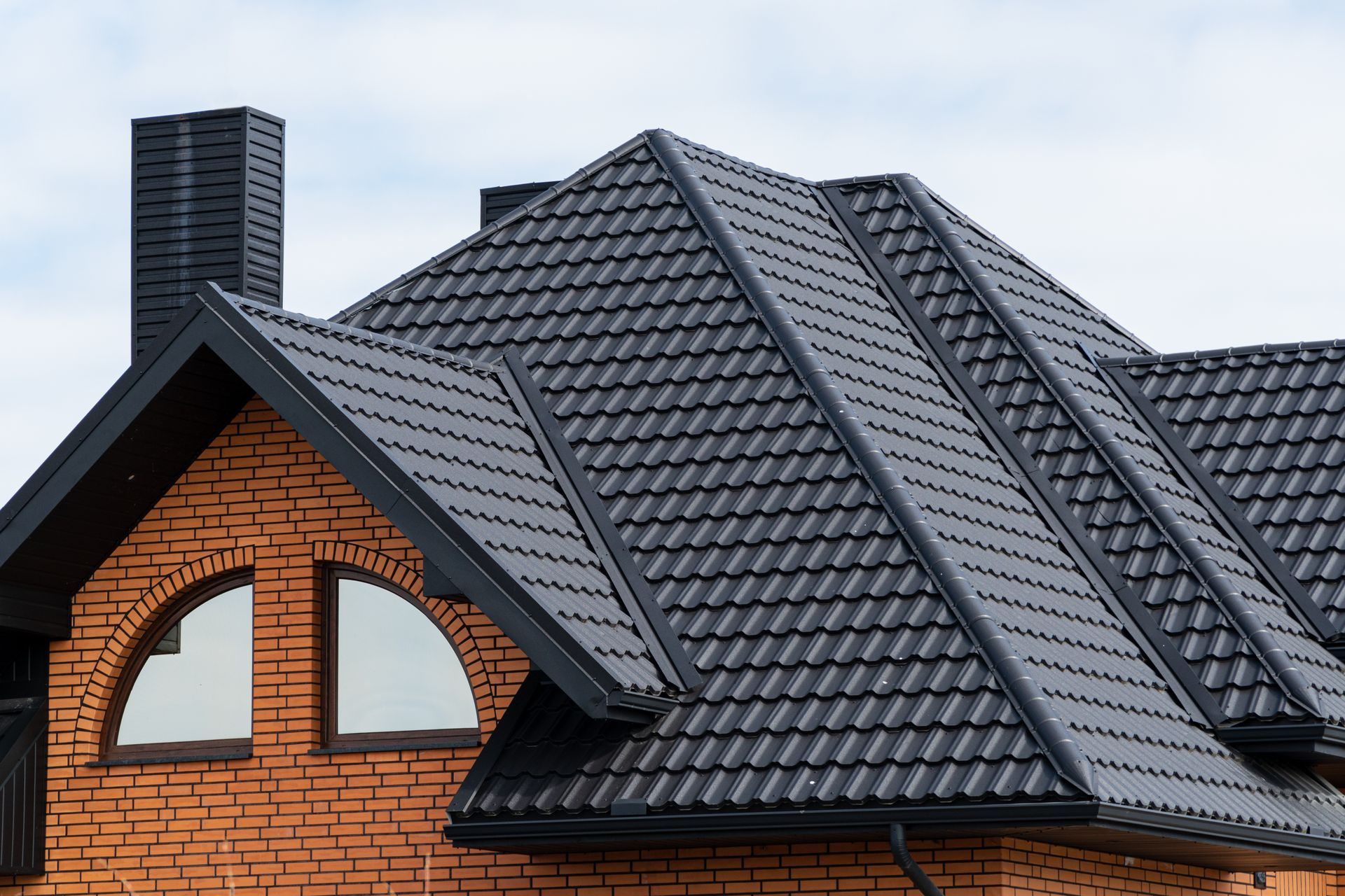 A brick house with a black roof and arched windows.