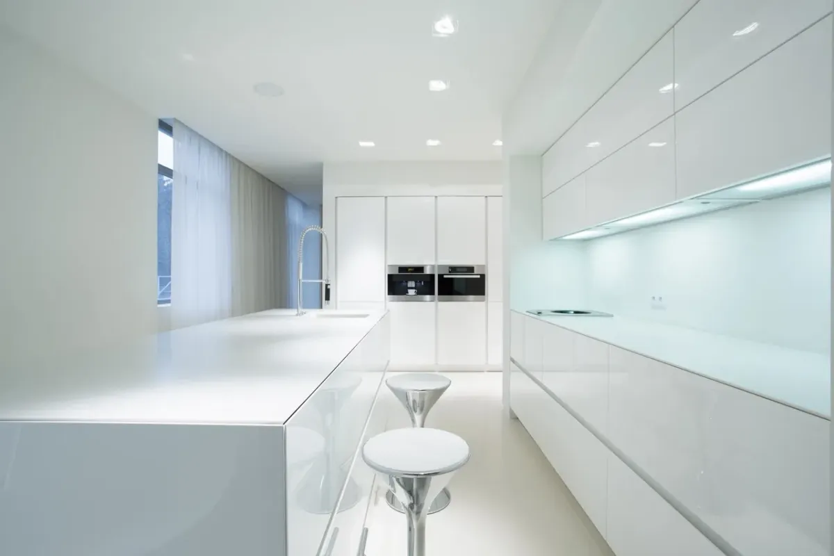 A kitchen with white cabinets , stools , and appliances.