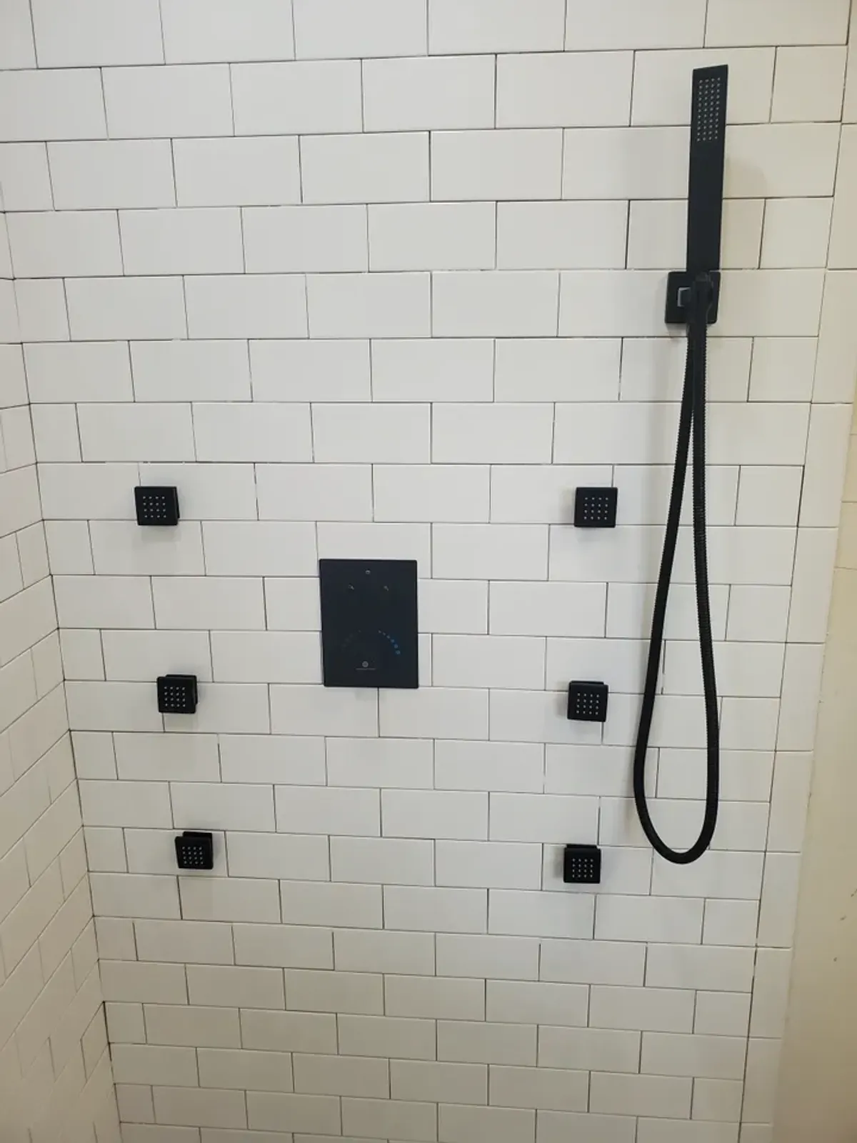 A black shower head is hanging from a white brick wall.