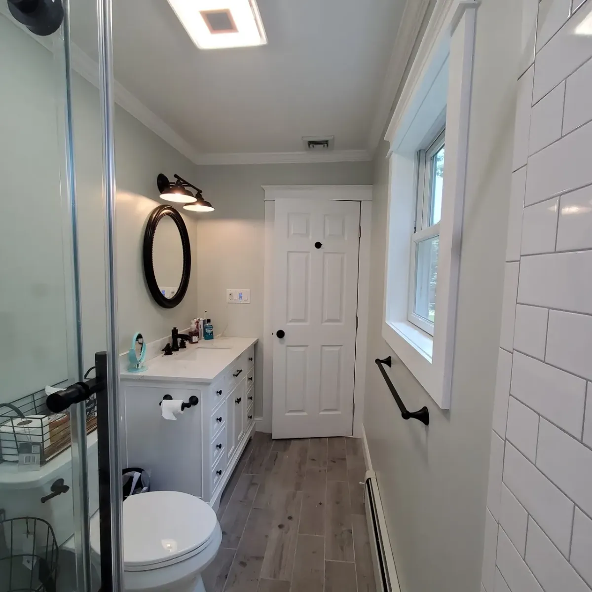A bathroom with a toilet , sink , mirror and window.