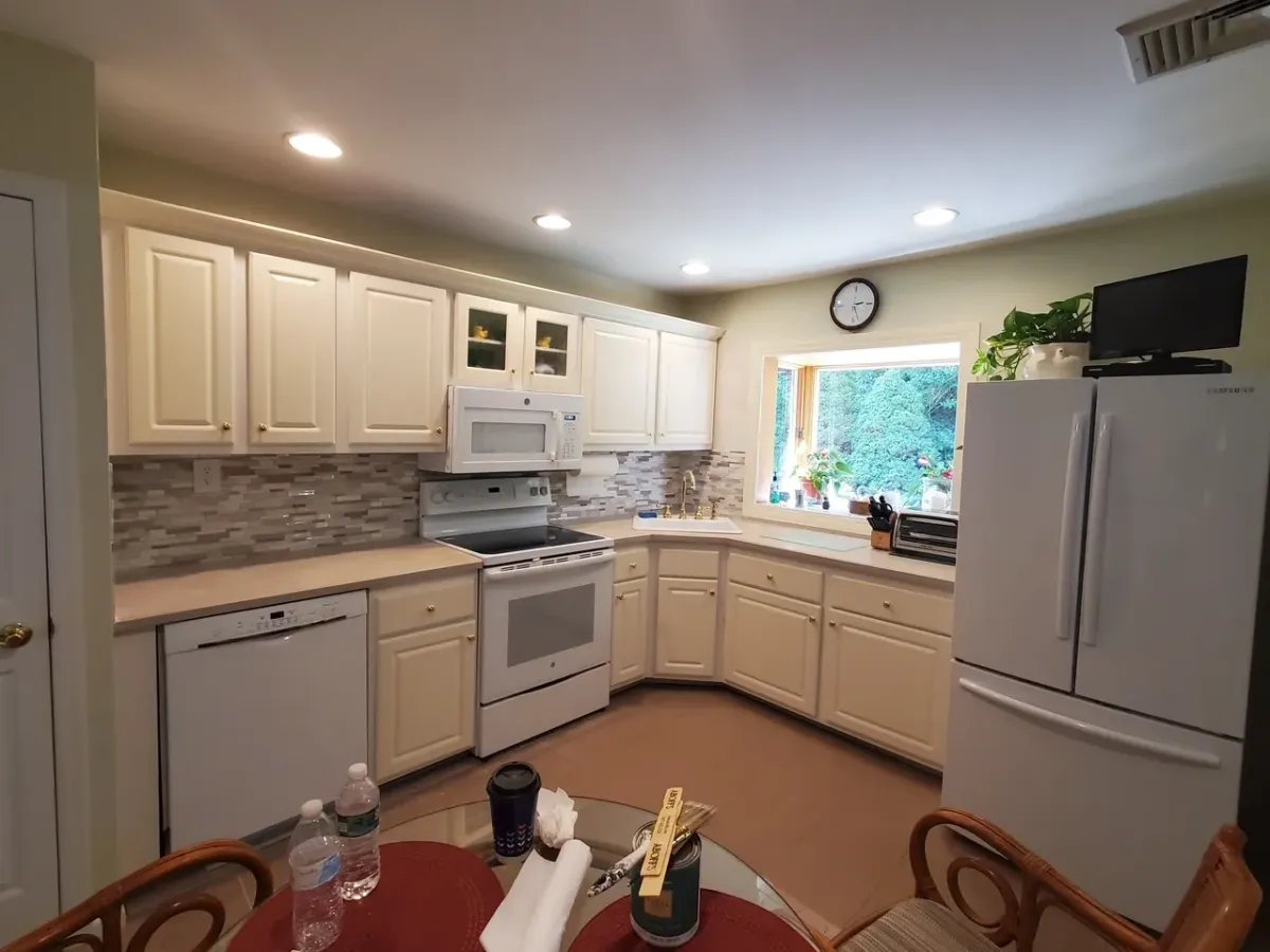 A kitchen with white cabinets , a stove , a refrigerator , a dishwasher , and a table.