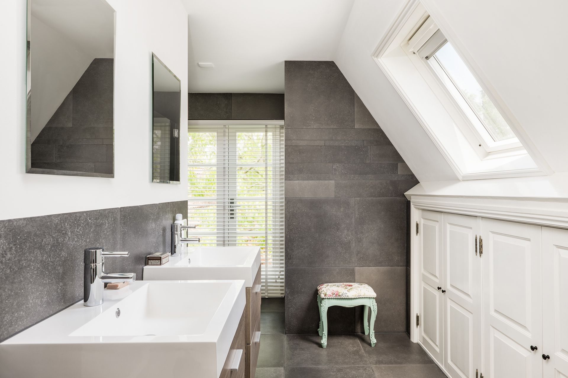 A bathroom with two sinks , two mirrors and a skylight.