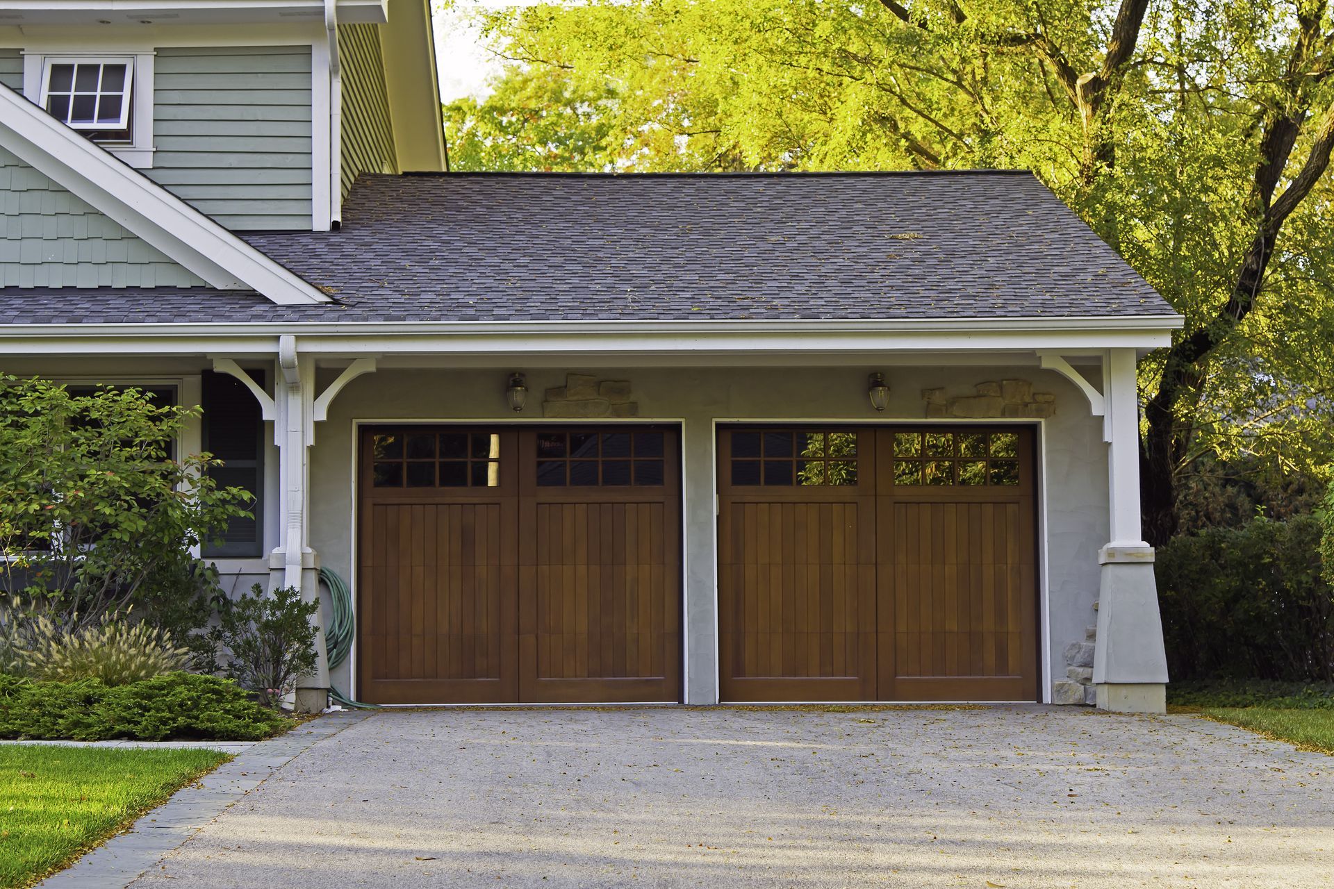 A house with two wooden garage doors and a gravel driveway