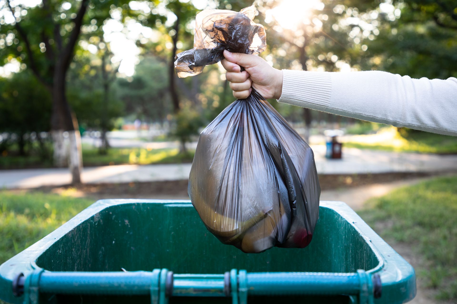 A person is throwing a garbage bag into a trash can.