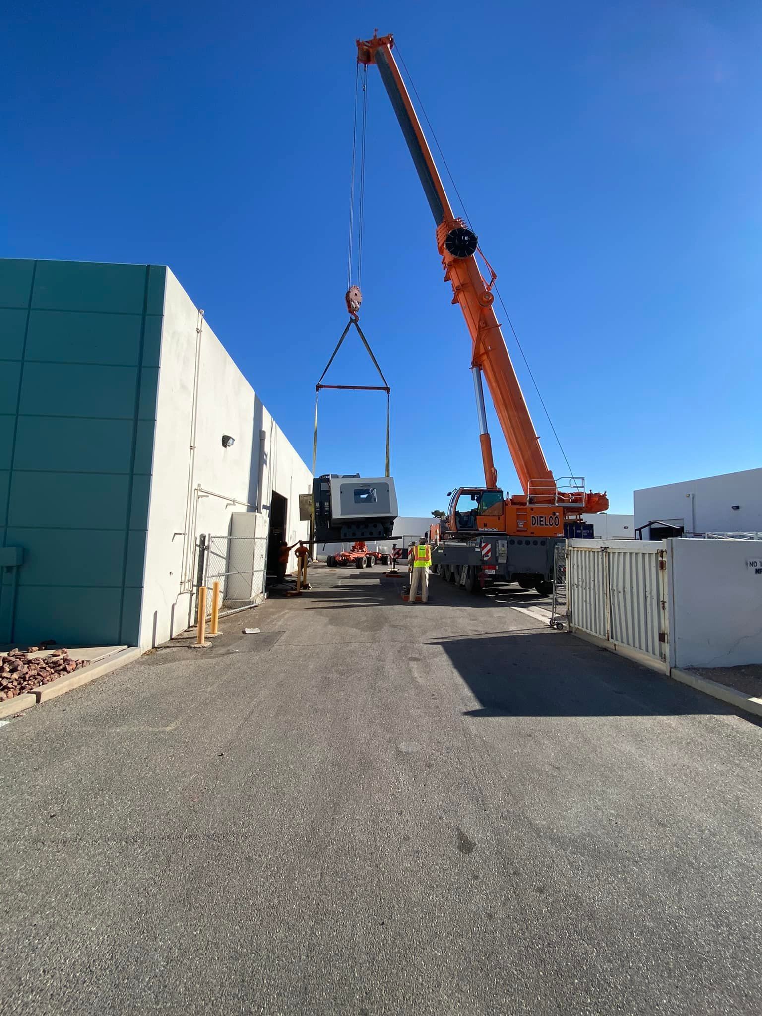 A large orange crane is lifting a large piece of equipment into a building.