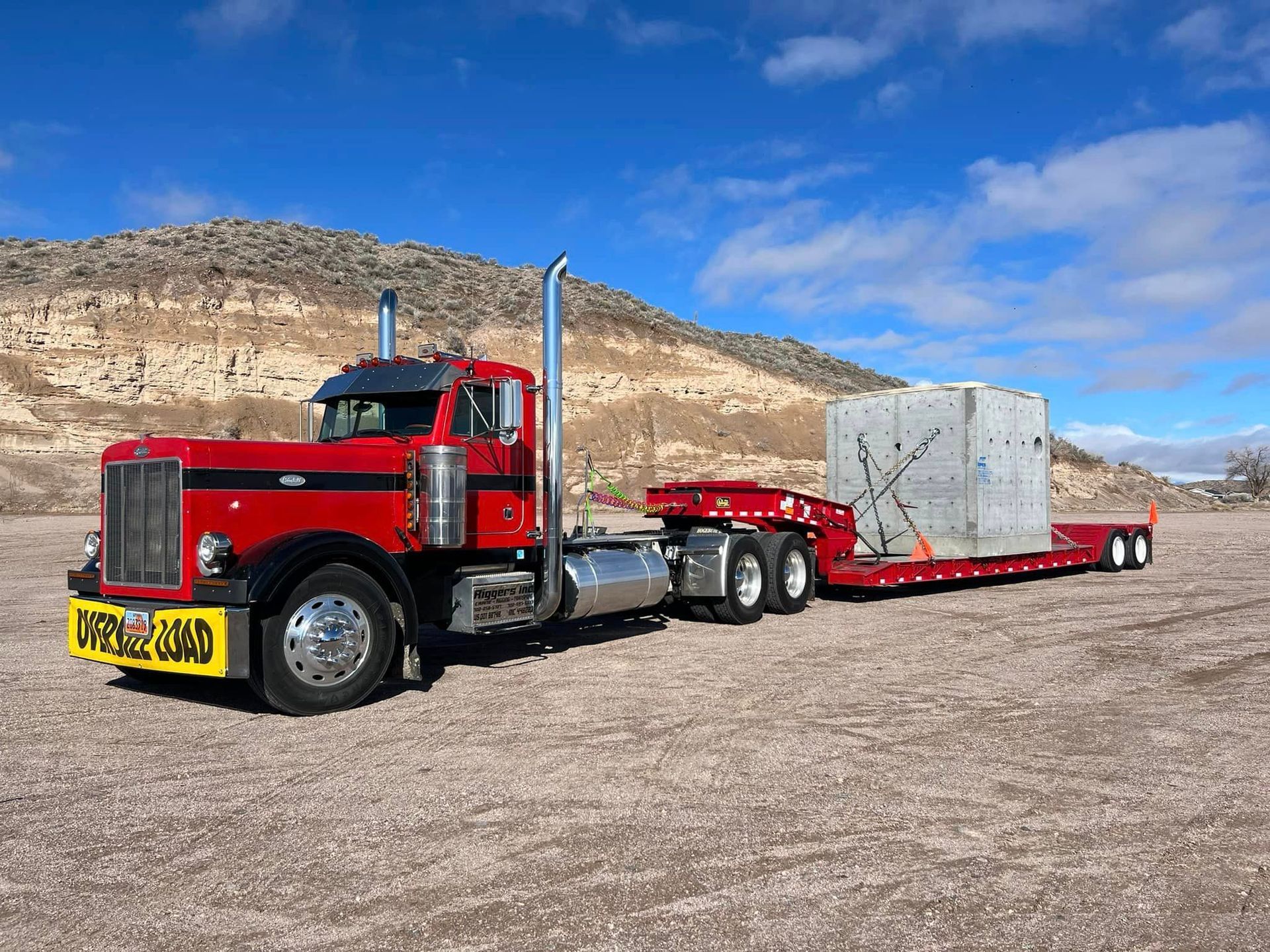 A red semi truck is carrying a large concrete block on a trailer.
