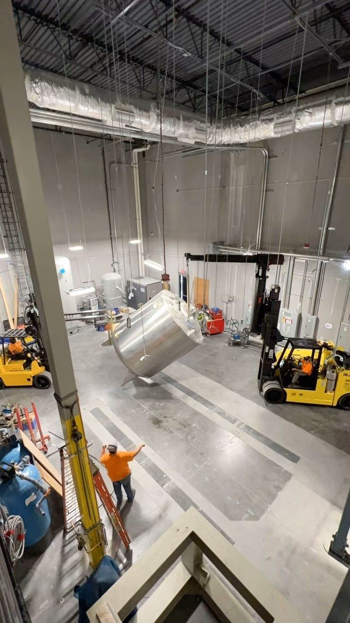 A large tank is being lifted by a crane in a warehouse.