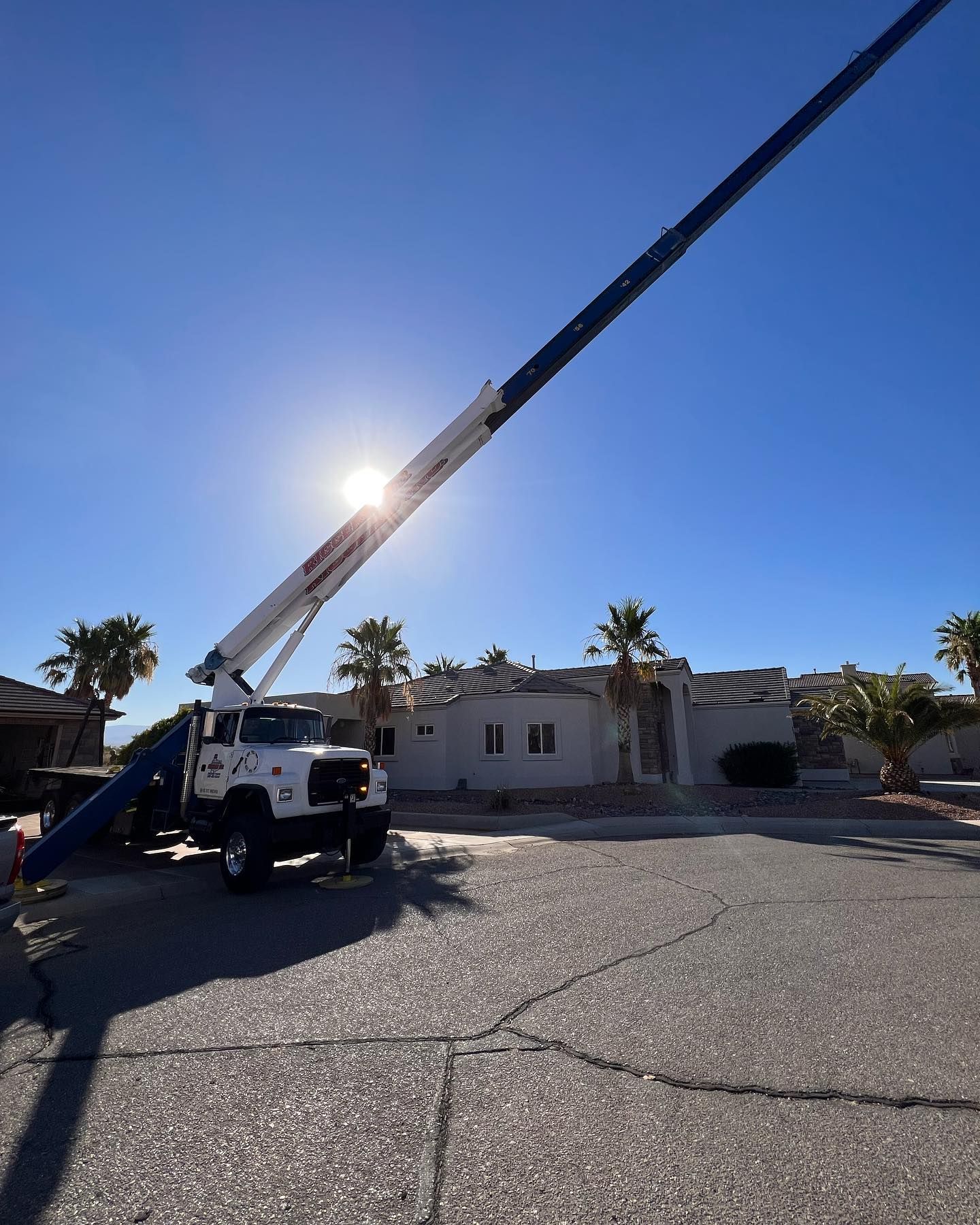 A white truck with a crane attached to it is parked in front of a house.