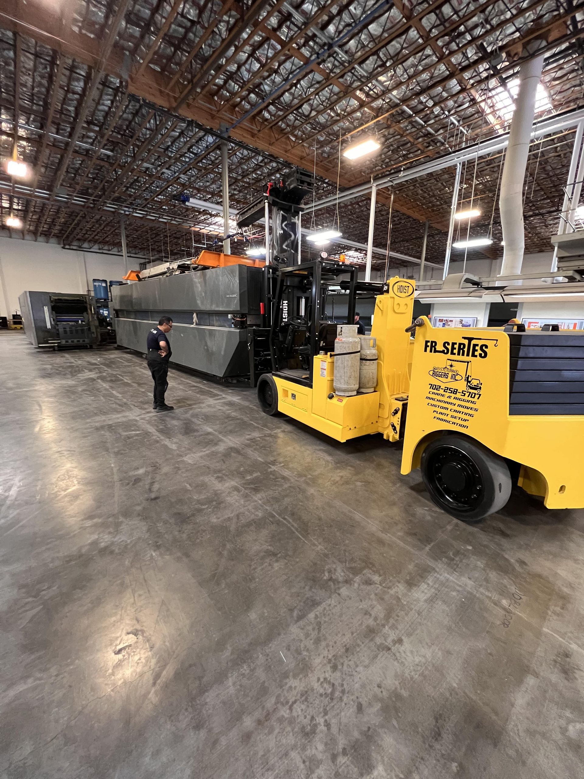 A man is standing next to a yellow forklift in a warehouse.