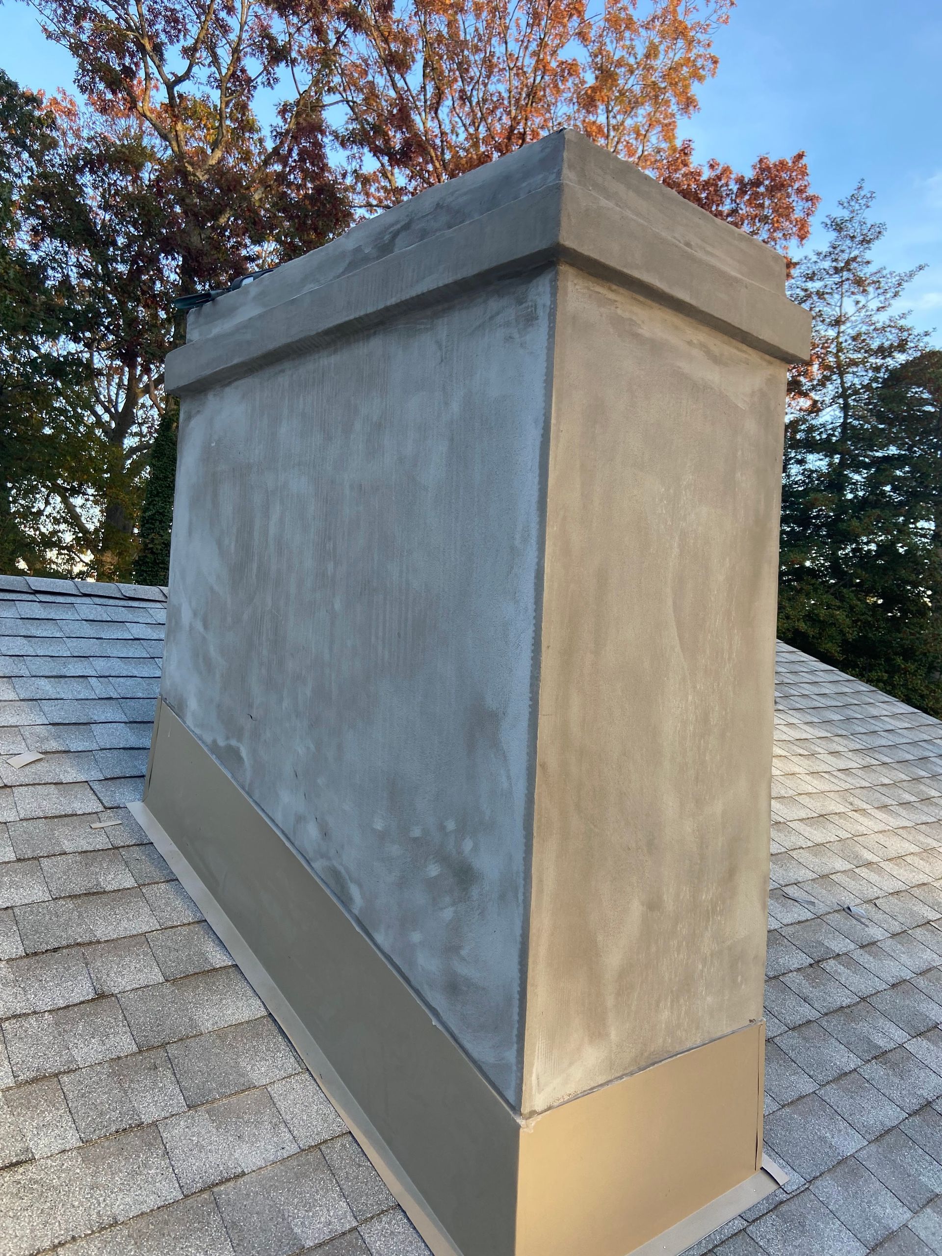 A chimney on top of a roof with trees in the background.
