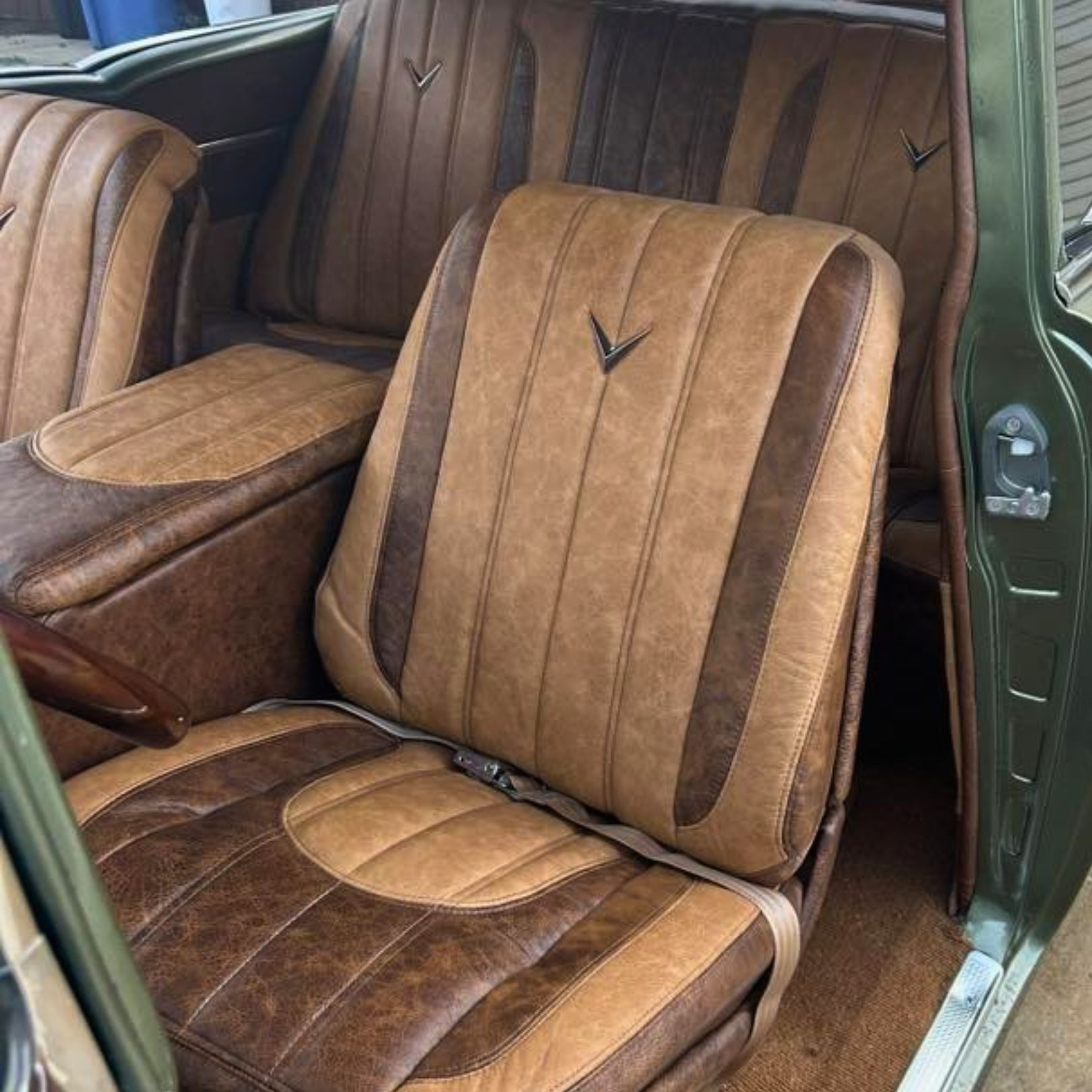 Car interior featuring custom-upholstered tan and dark brown leather bucket seats with a central emblem.