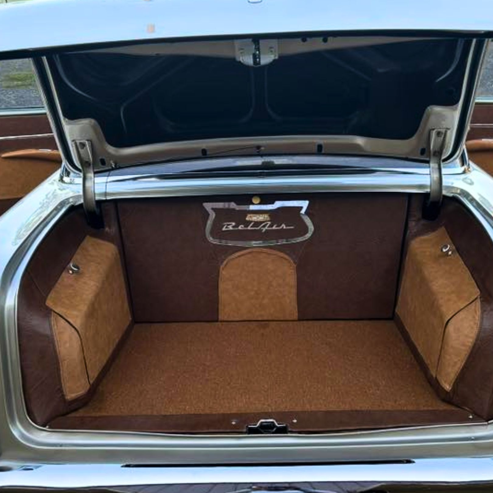 The open trunk of a vintage Chevrolet Bel Air, featuring custom brown and tan upholstery and a chrome