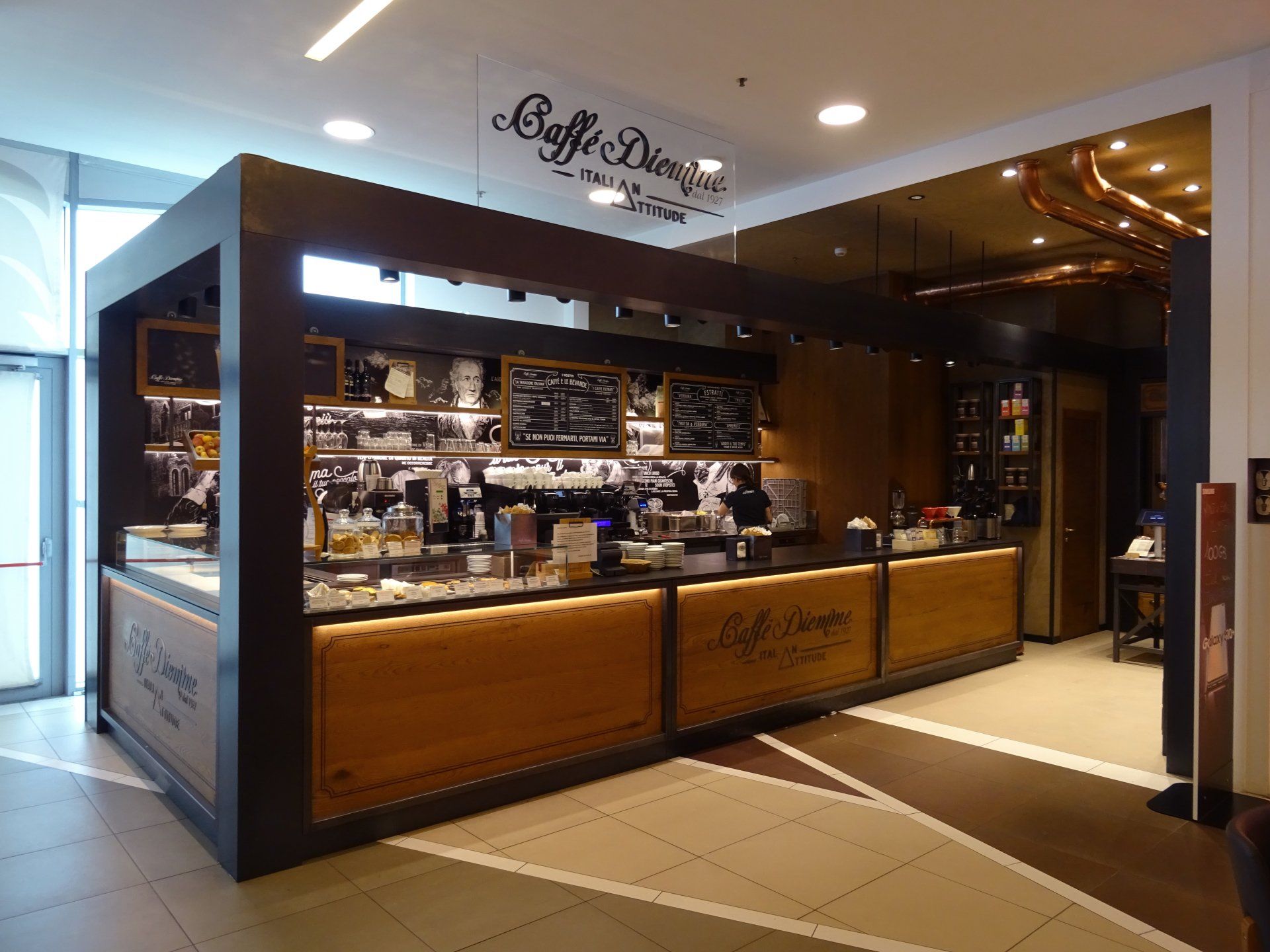 Una caffetteria all'interno di un centro commerciale con un grande bancone in legno.