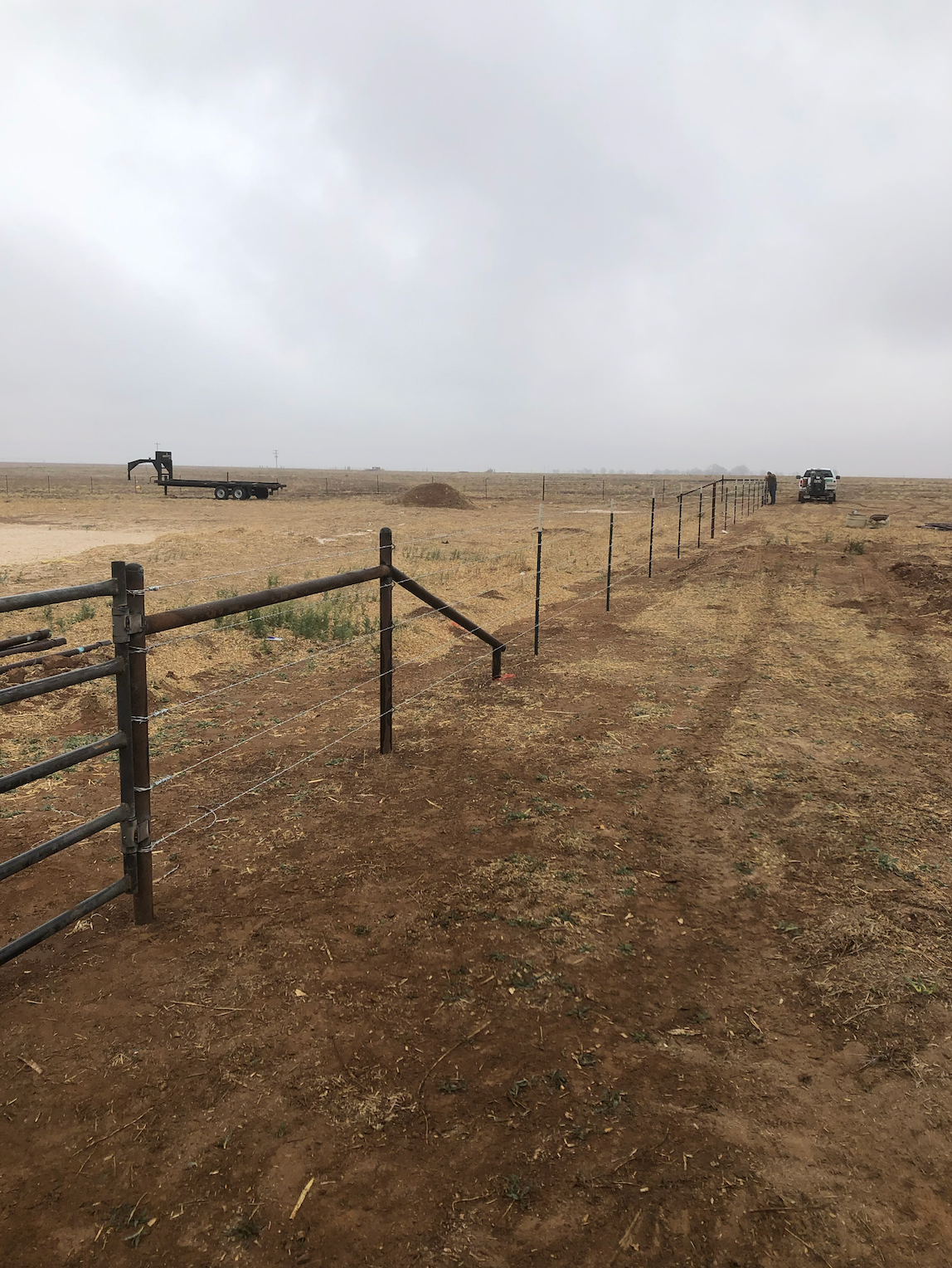 There is a fence in the middle of a dirt field.