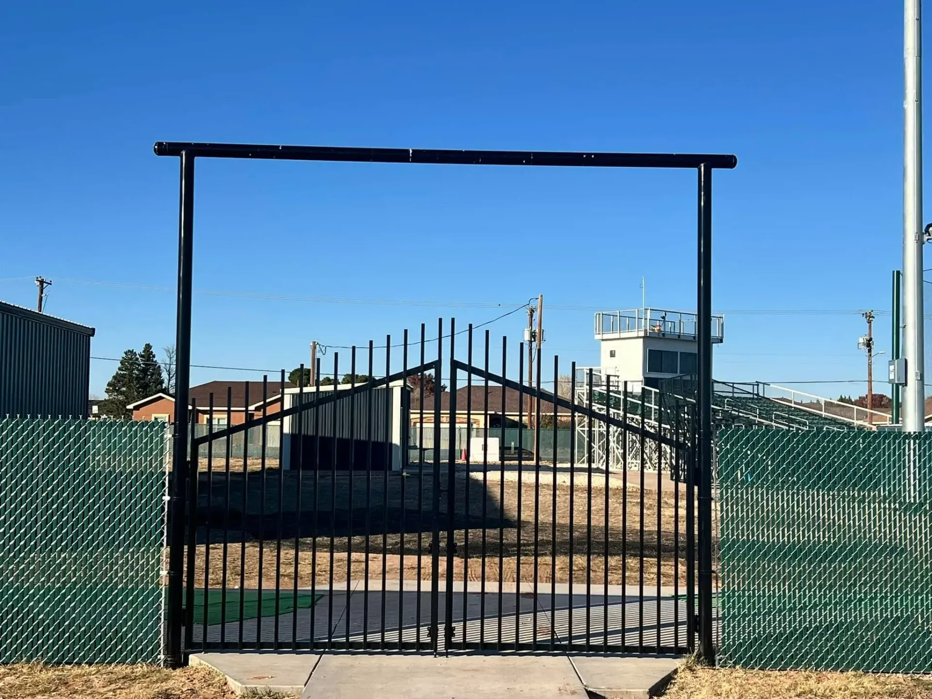 A black gate with a green fence behind it