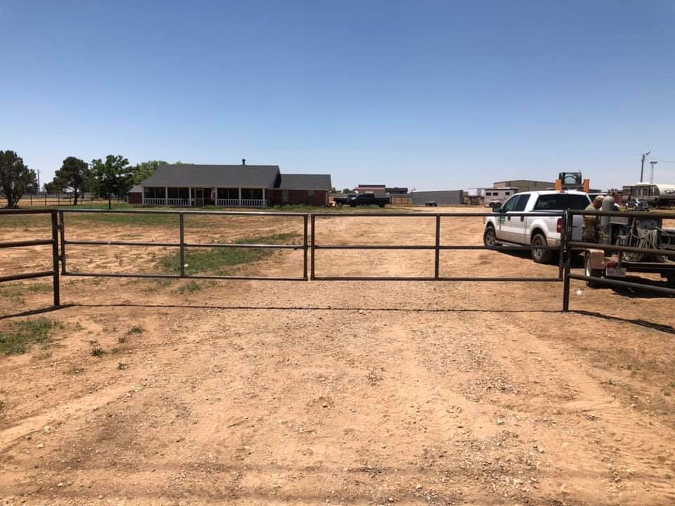 A dirt road with a fence and a house in the background.