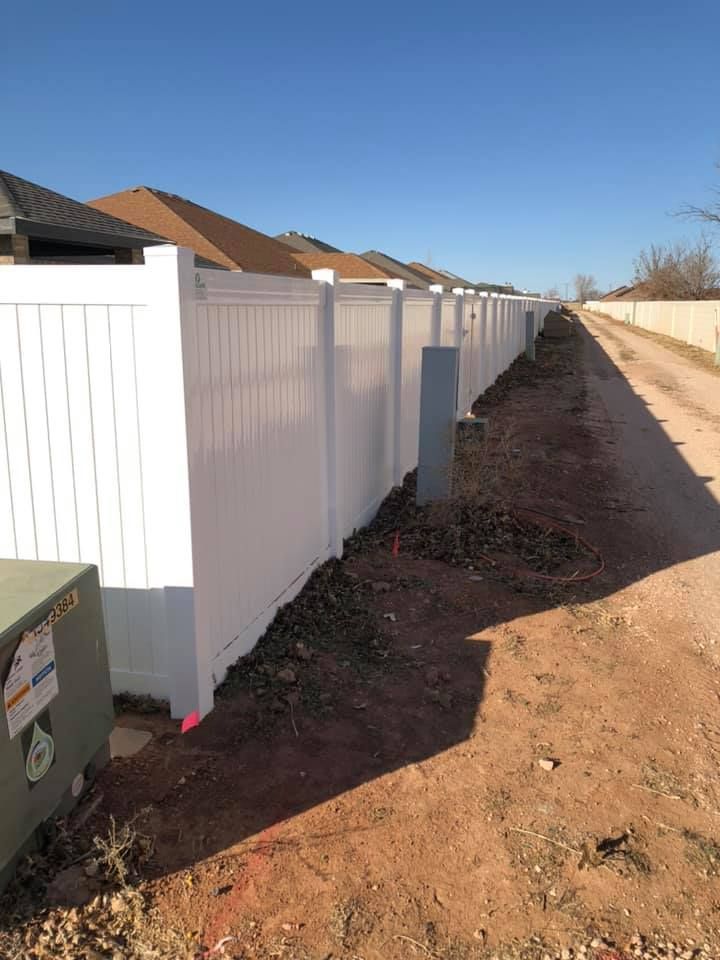 A white fence is along the side of a dirt road.