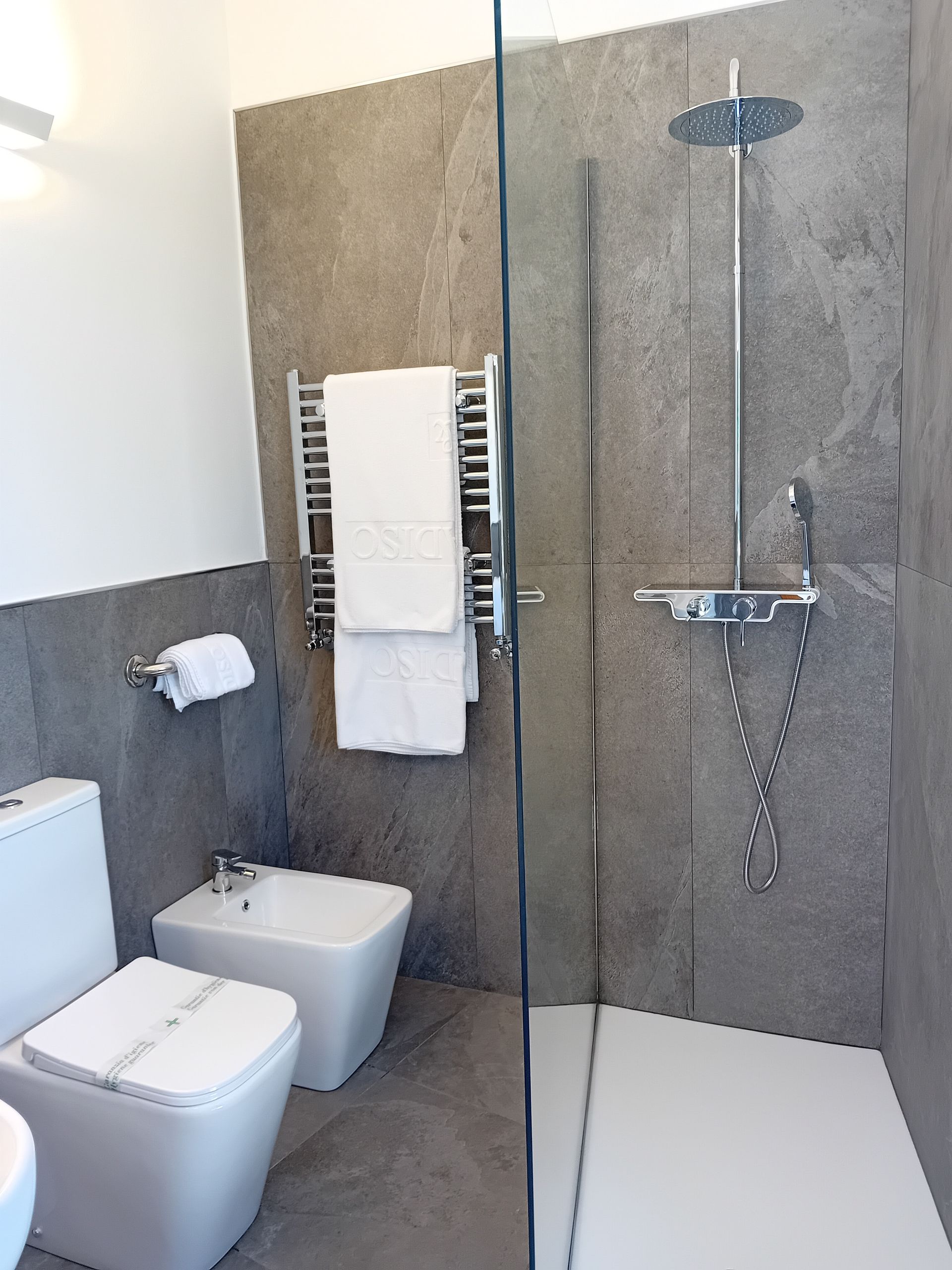 Bagno moderno con cabina doccia, WC, bidet e scaldasalviette. Pareti e pavimenti in pietra grigia.