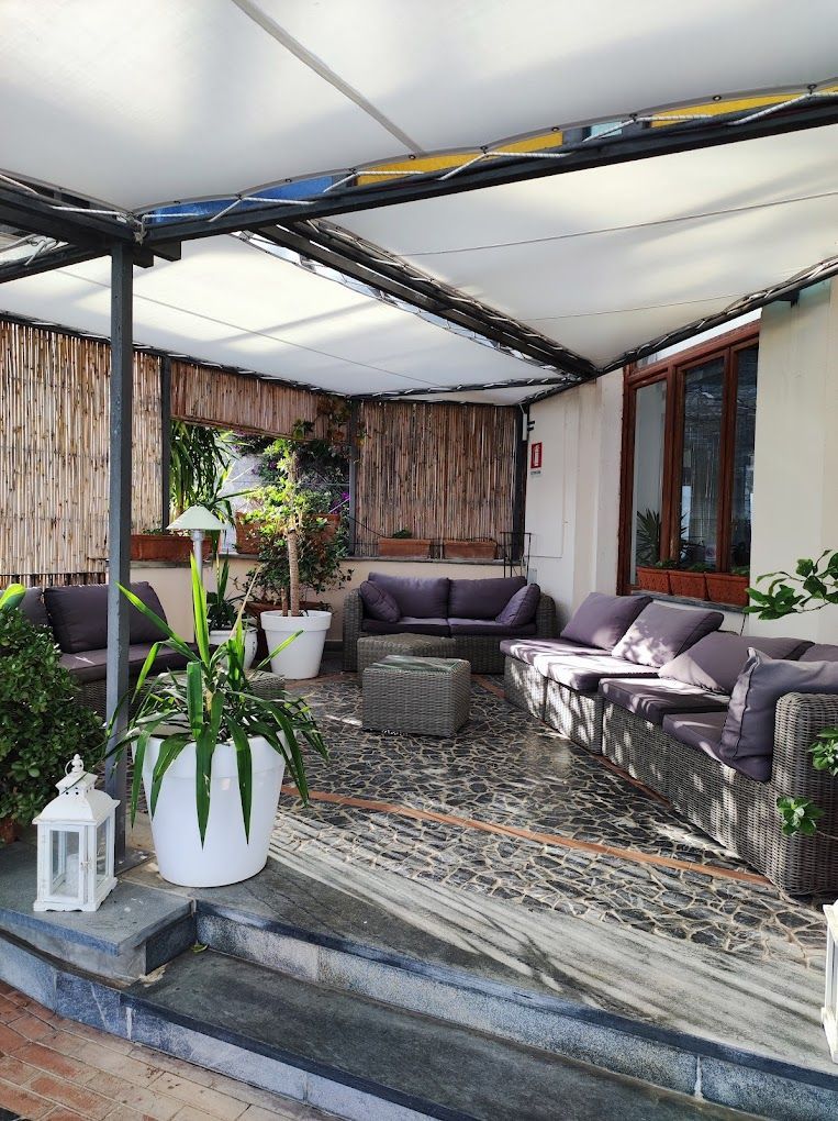 Area salotto all'aperto con divani, piante e patio coperto.