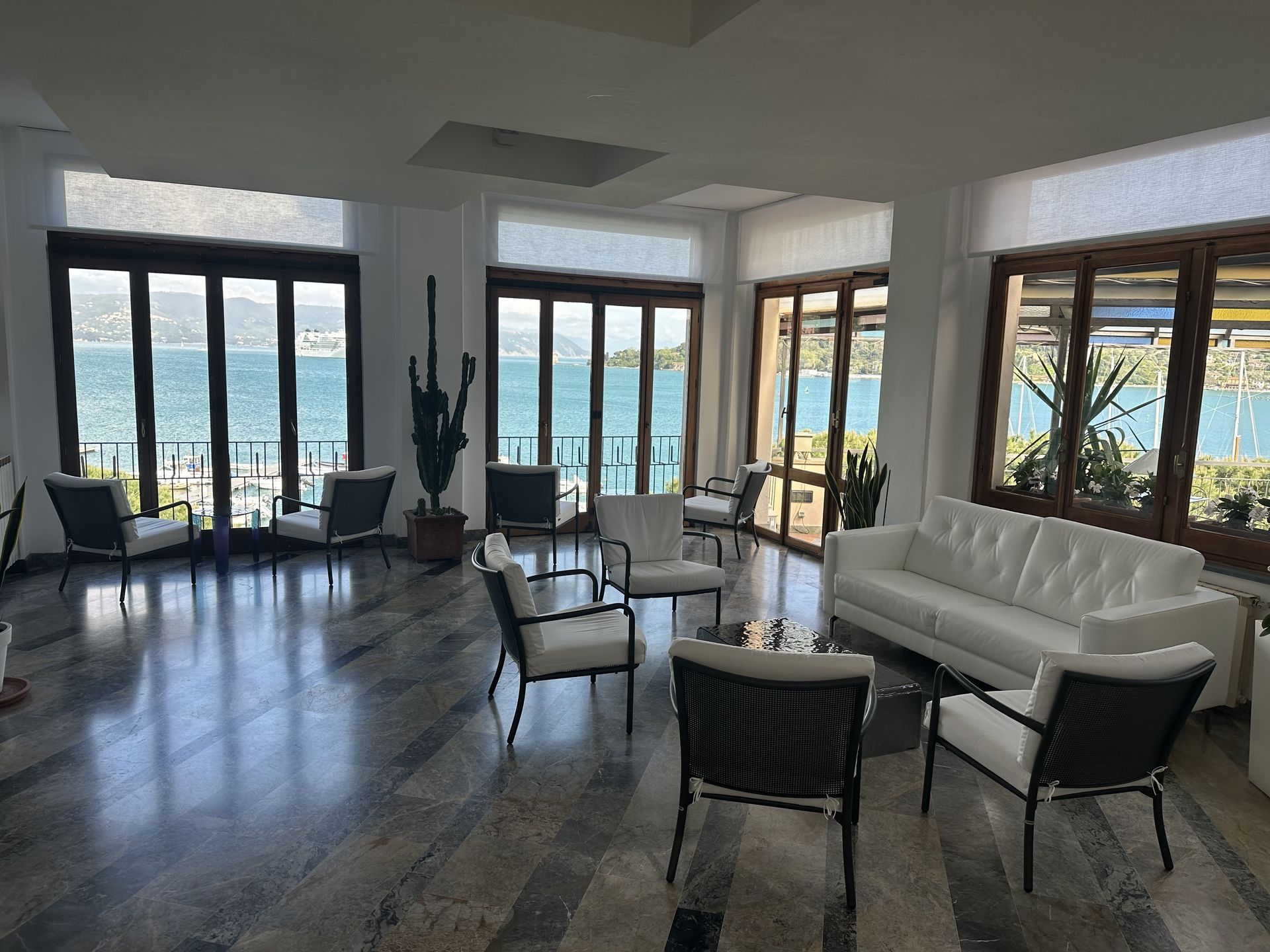Zona lounge con mobili bianchi e ampie finestre con vista sul lago blu.