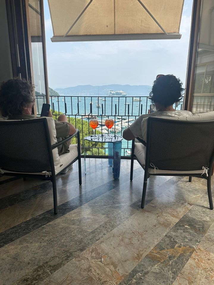 Due persone sedute su un balcone sorseggiano un drink ammirando la vista panoramica sull'oceano.