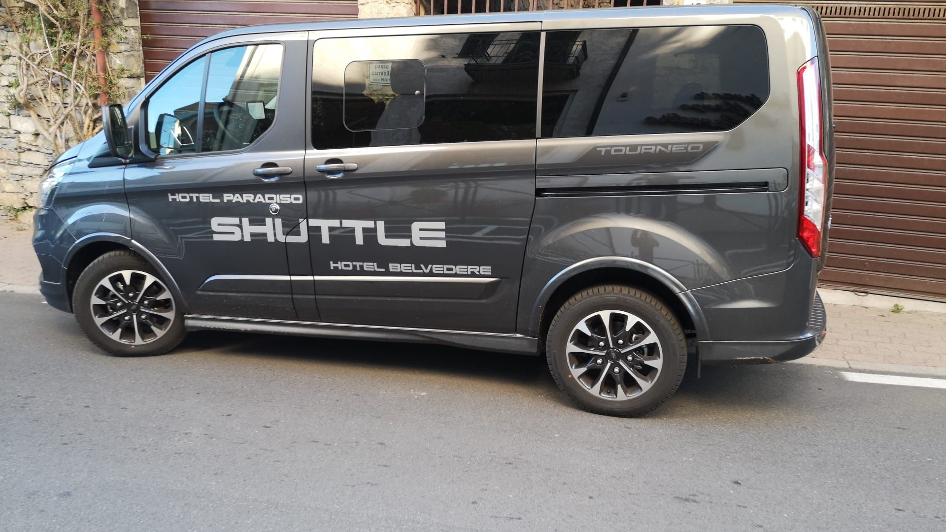 Furgone navetta grigio parcheggiato su una strada; il testo dice 