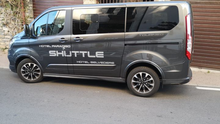 Furgone navetta grigio parcheggiato su una strada; il testo dice 