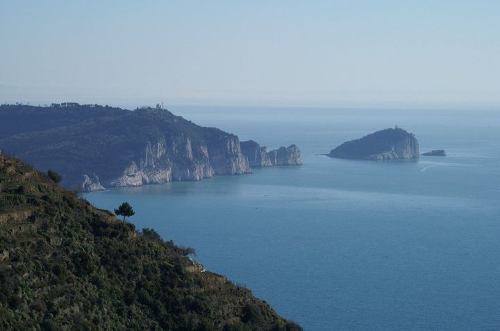 Vista sull'oceano azzurro con scogliere rocciose e una piccola isola sotto un cielo limpido.