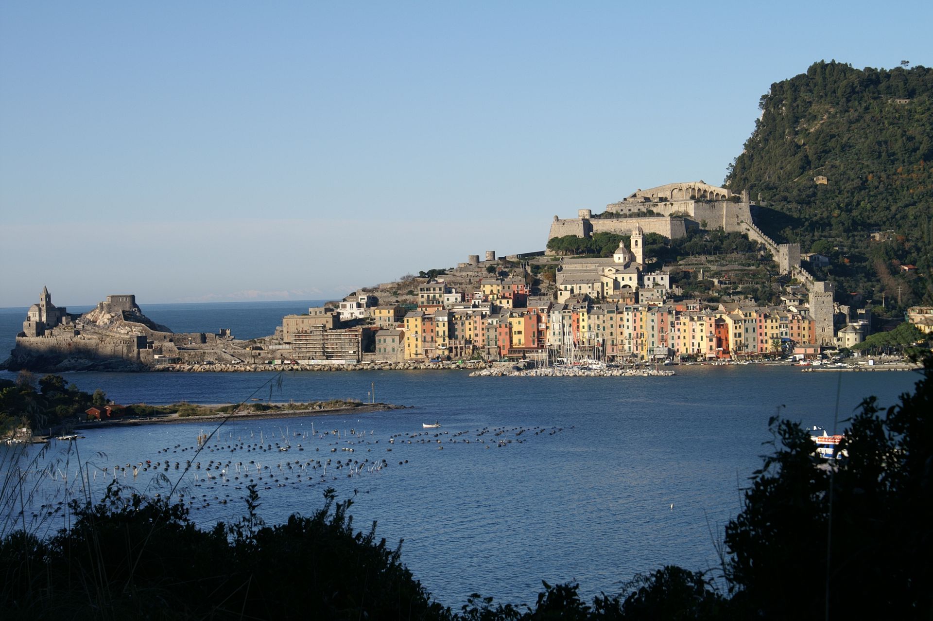Porto Venere, cittadina costiera italiana, con edifici colorati, castello e mare.
