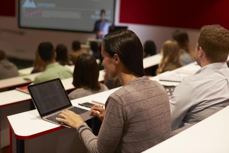 A group of people are sitting in a lecture hall using laptops.