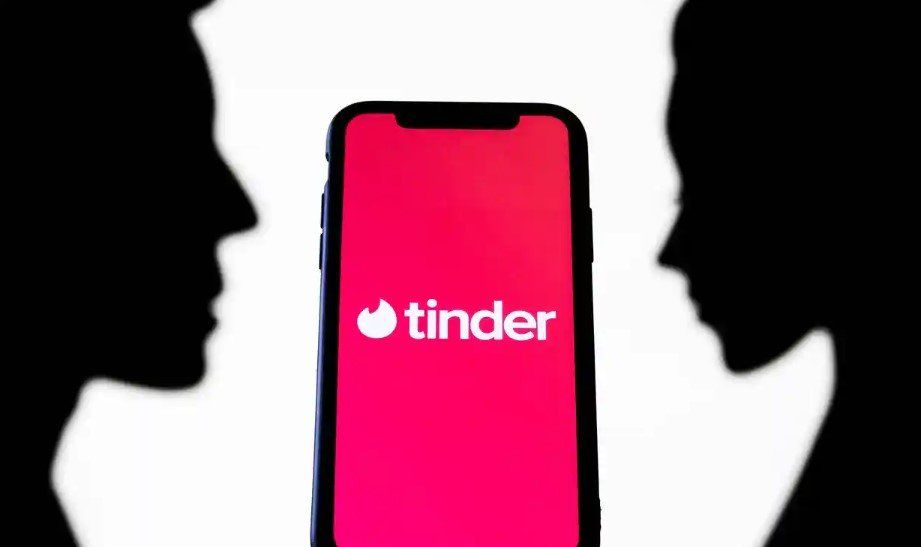 A silhouette of two people looking at a tinder app on a cell phone.