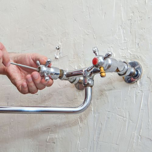 Spring Creek Water & Plumbing Services - A person is fixing a faucet with a wrench.