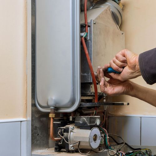 Spring Creek Water  Plumbing Services - A person is fixing a boiler with a screwdriver.