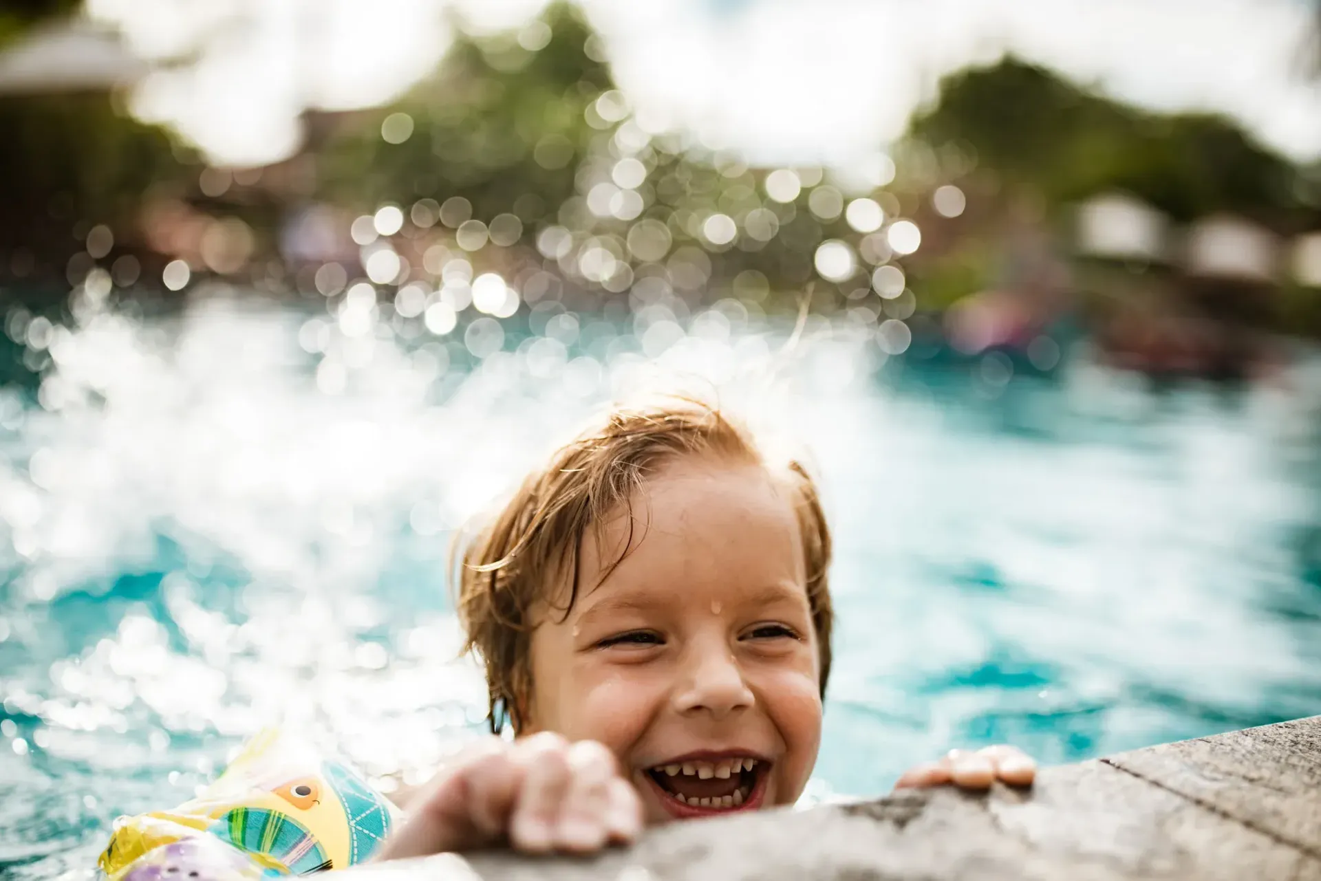 A young boy is swimming in a swimming pool and smiling.