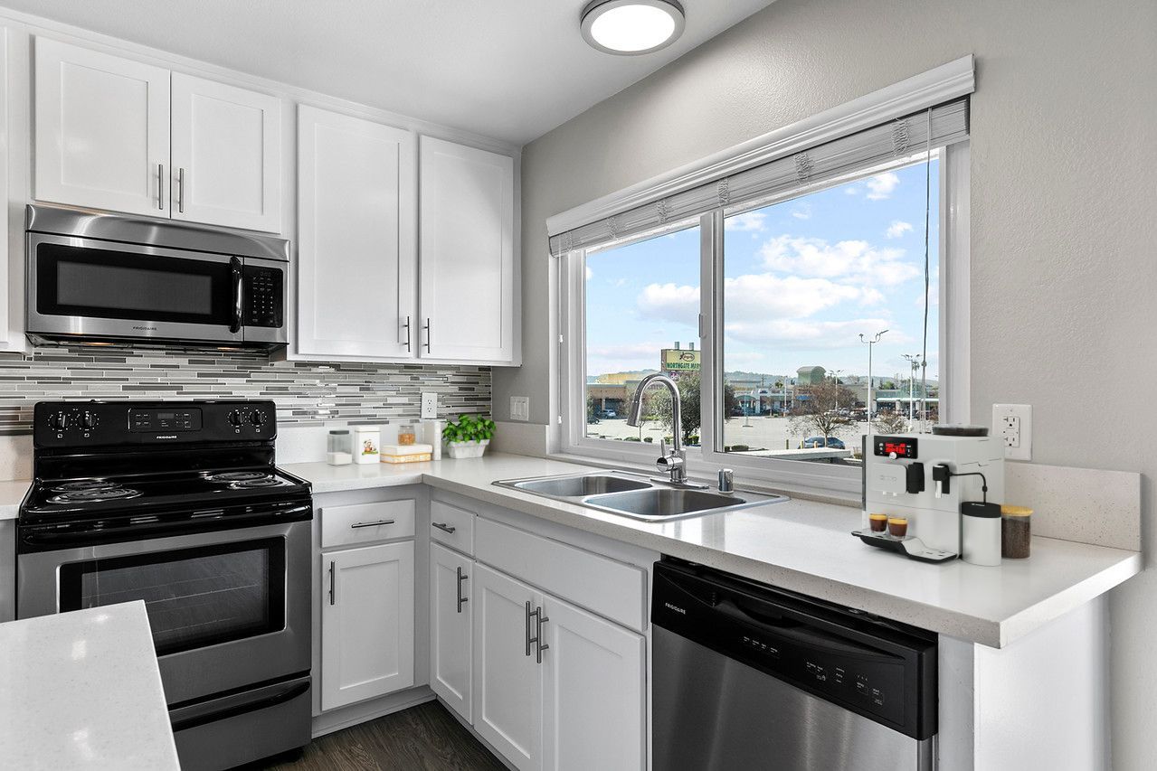 A kitchen with white cabinets , stainless steel appliances and a large window.