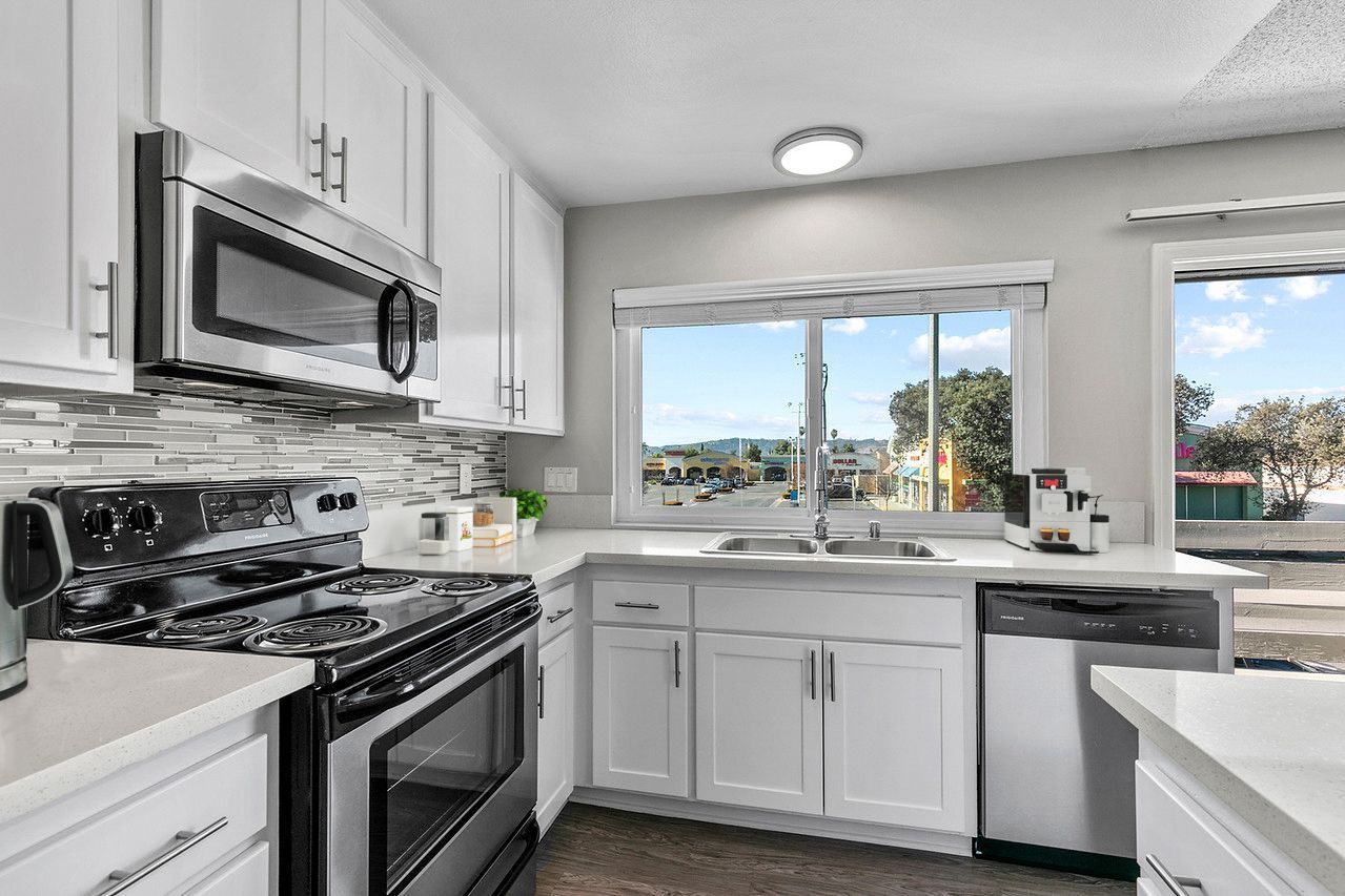 A kitchen with white cabinets , stainless steel appliances , a sink , and a window.