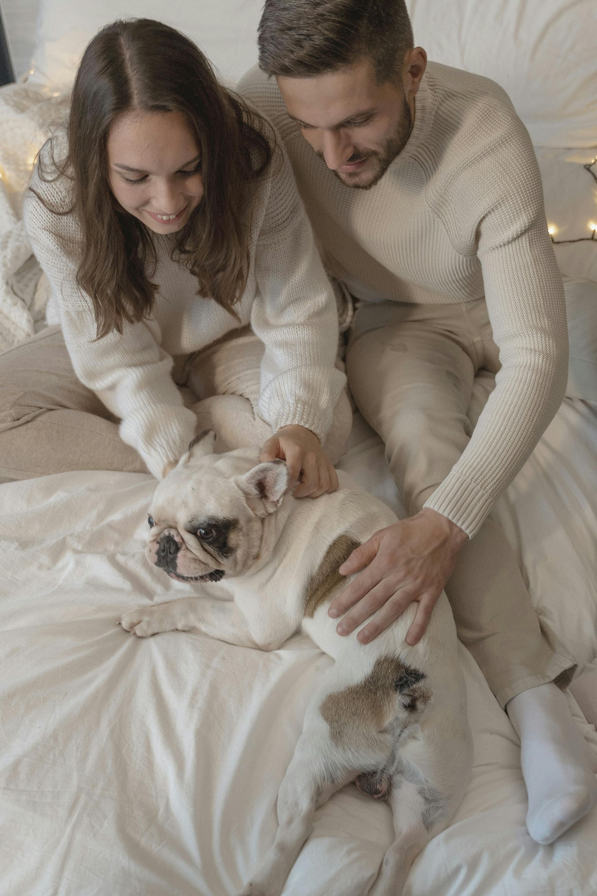A man and a woman are petting a dog on a bed.