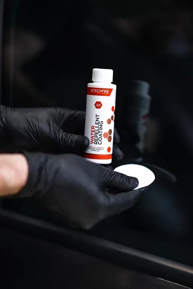 Gloved hands holding a small red-and-white bottle and a white cap in a dark car interior