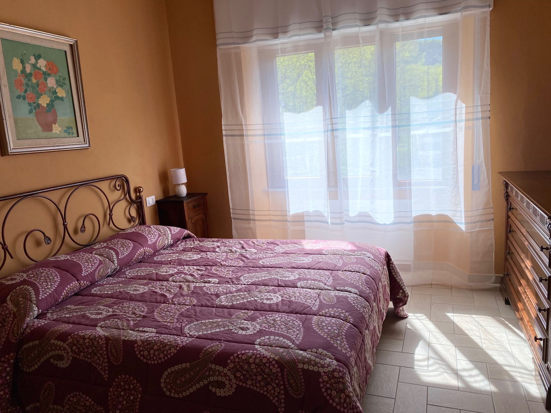 A bedroom with a bed, dresser, window, and a painting on the wall.