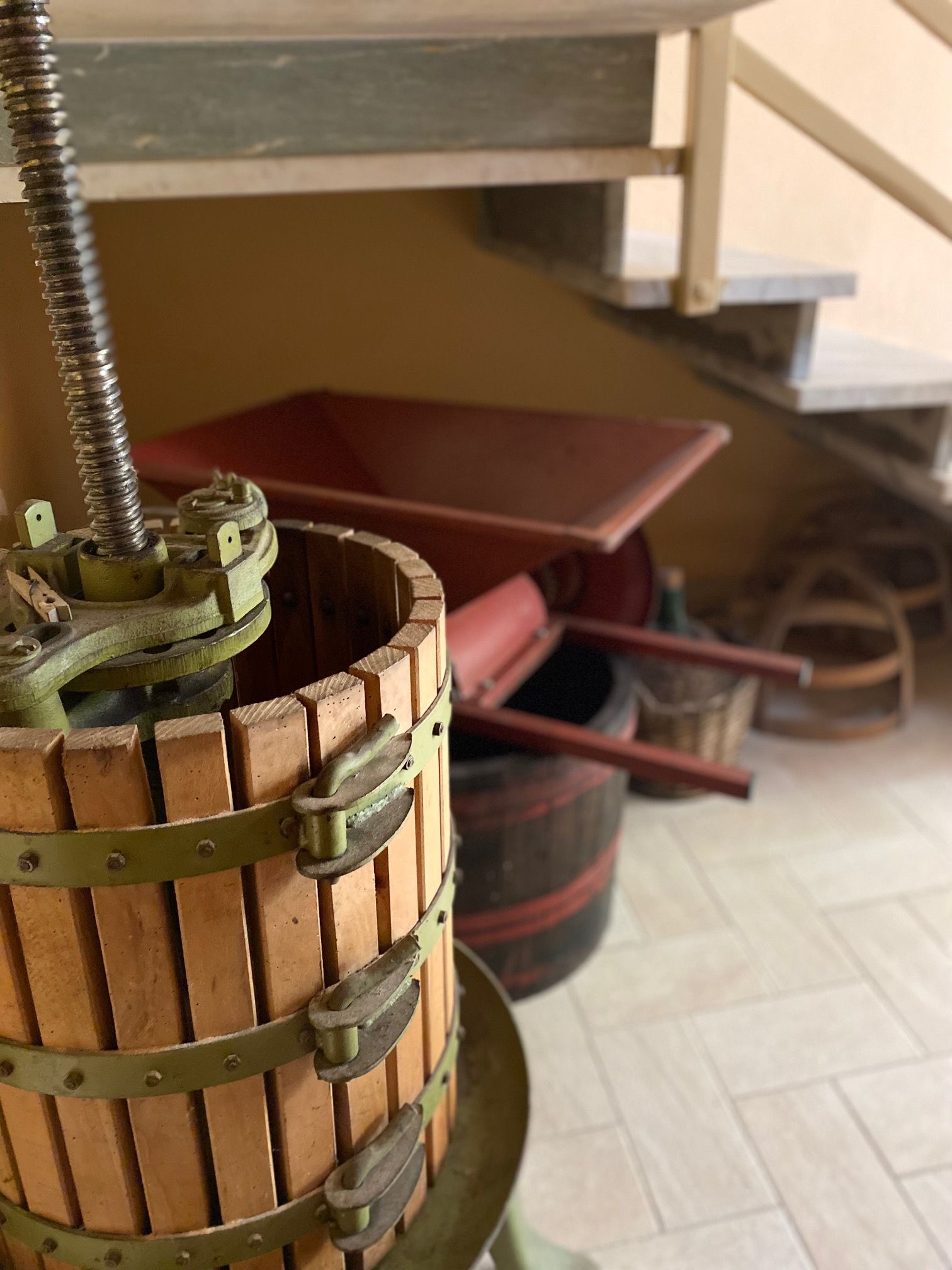 A wooden barrel with a metal handle is located in a room with stairs in the background.