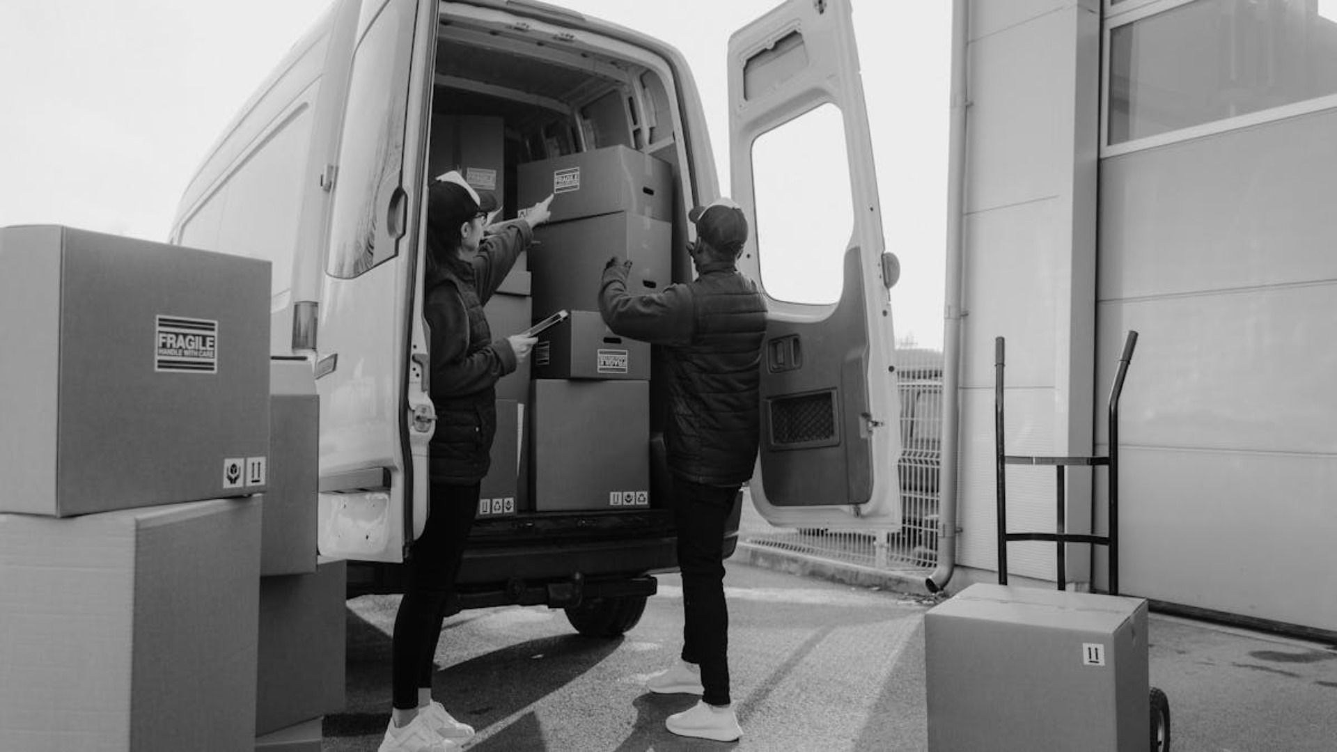 Dos personas cargando cajas de cartón en un camión de reparto, al aire libre.