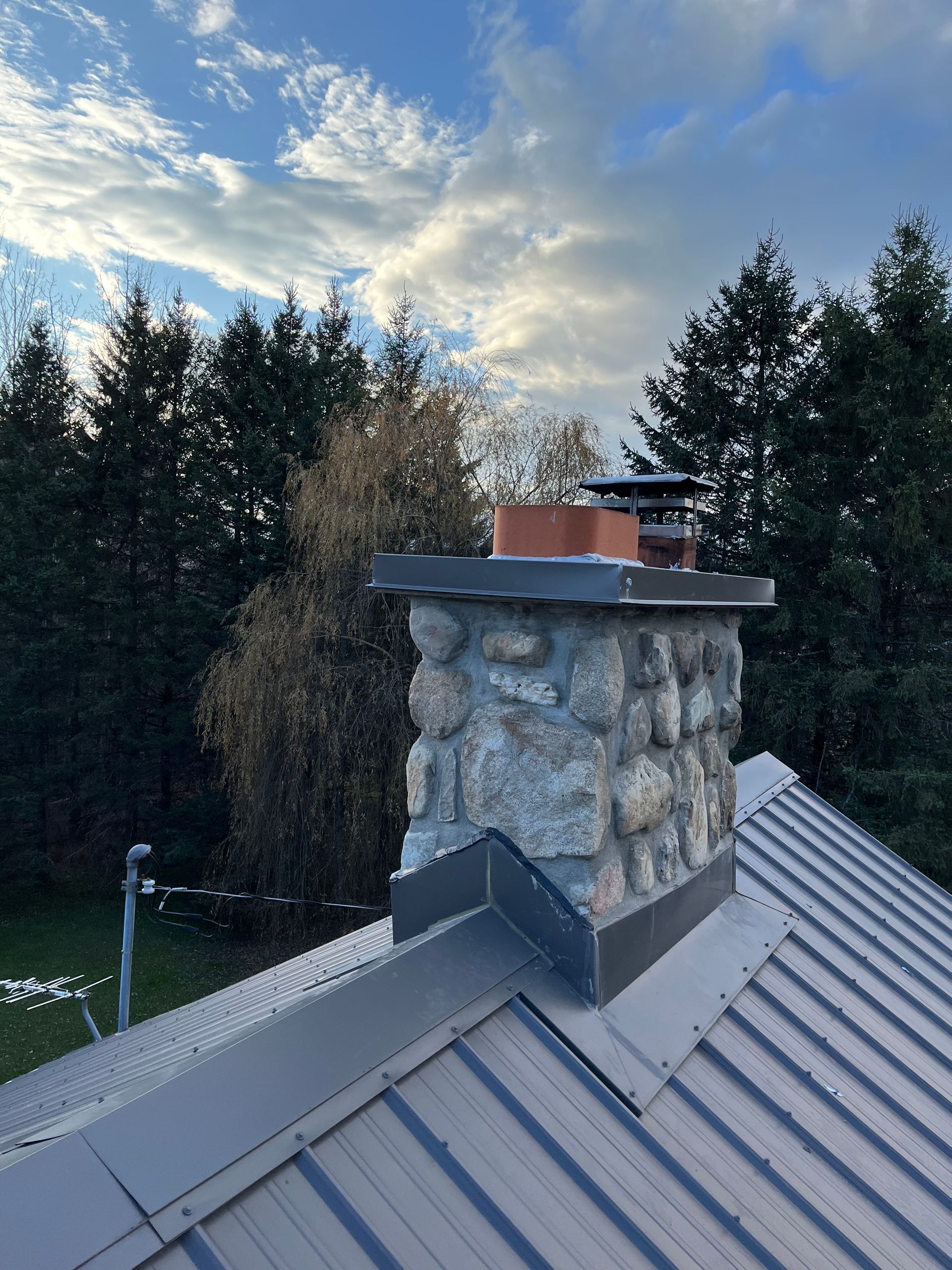Une cheminée au sommet d'un toit métallique avec des arbres en arrière-plan.